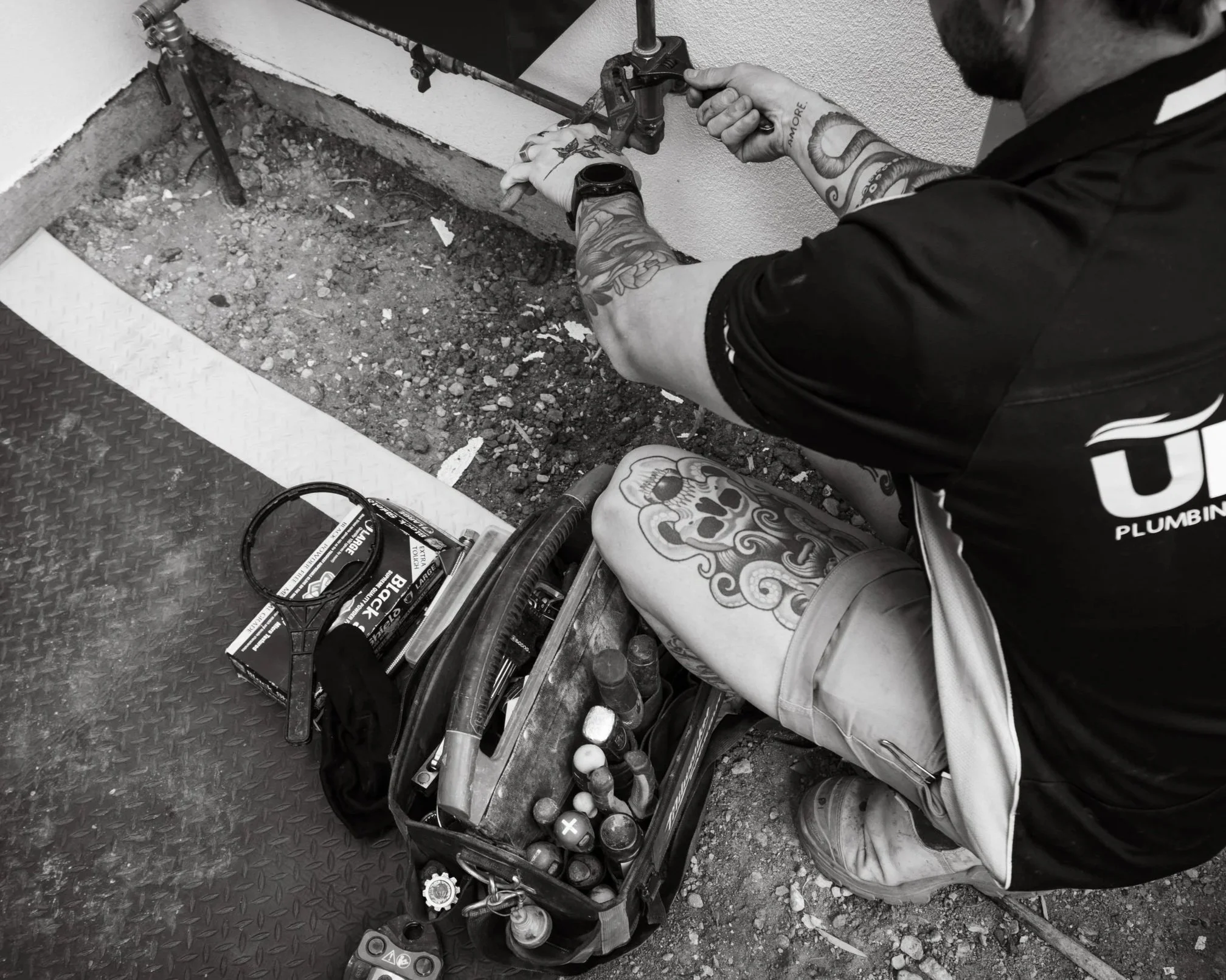 A plumber is working on new filtration system in a construction or repair setting. The task area is a small trench with exposed dirt. There is a toolbox and plumbing tools nearby.