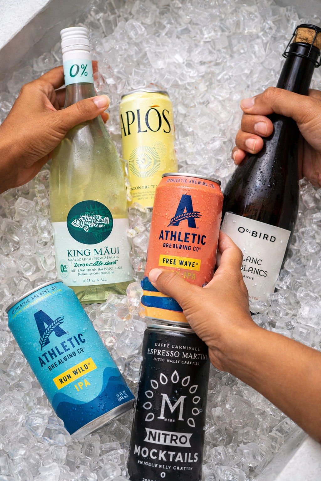 Multiple beverages including cans and bottles placed on ice, with two hands holding a bottle and a can.