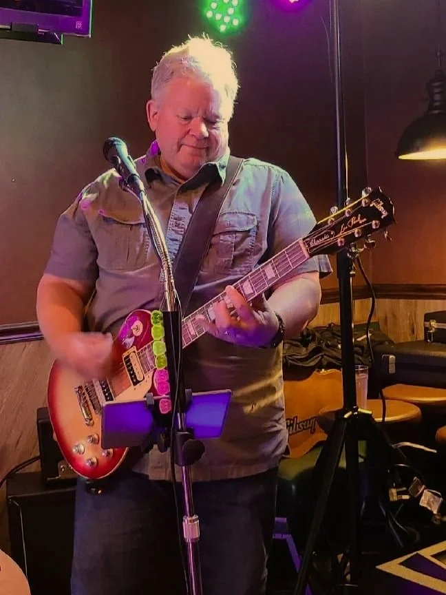 A person playing an electric guitar on stage with colorful stage lighting.