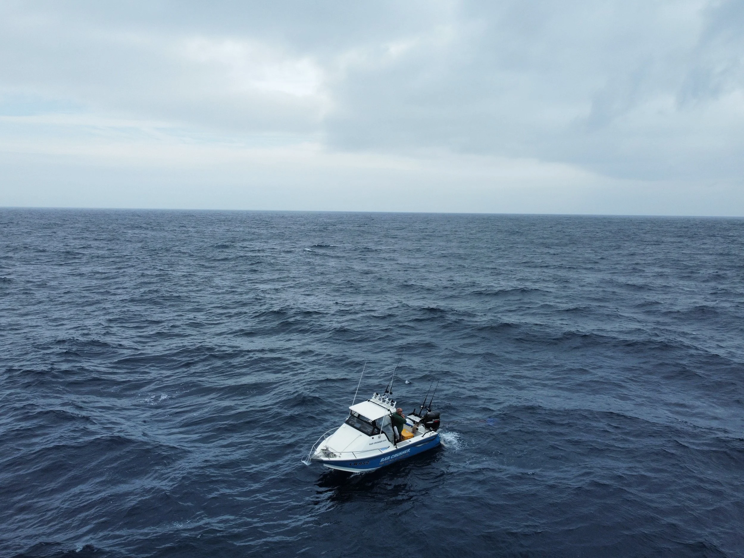 A small white and blue fishing boat sailing on the open ocean with cloudy skies overhead.