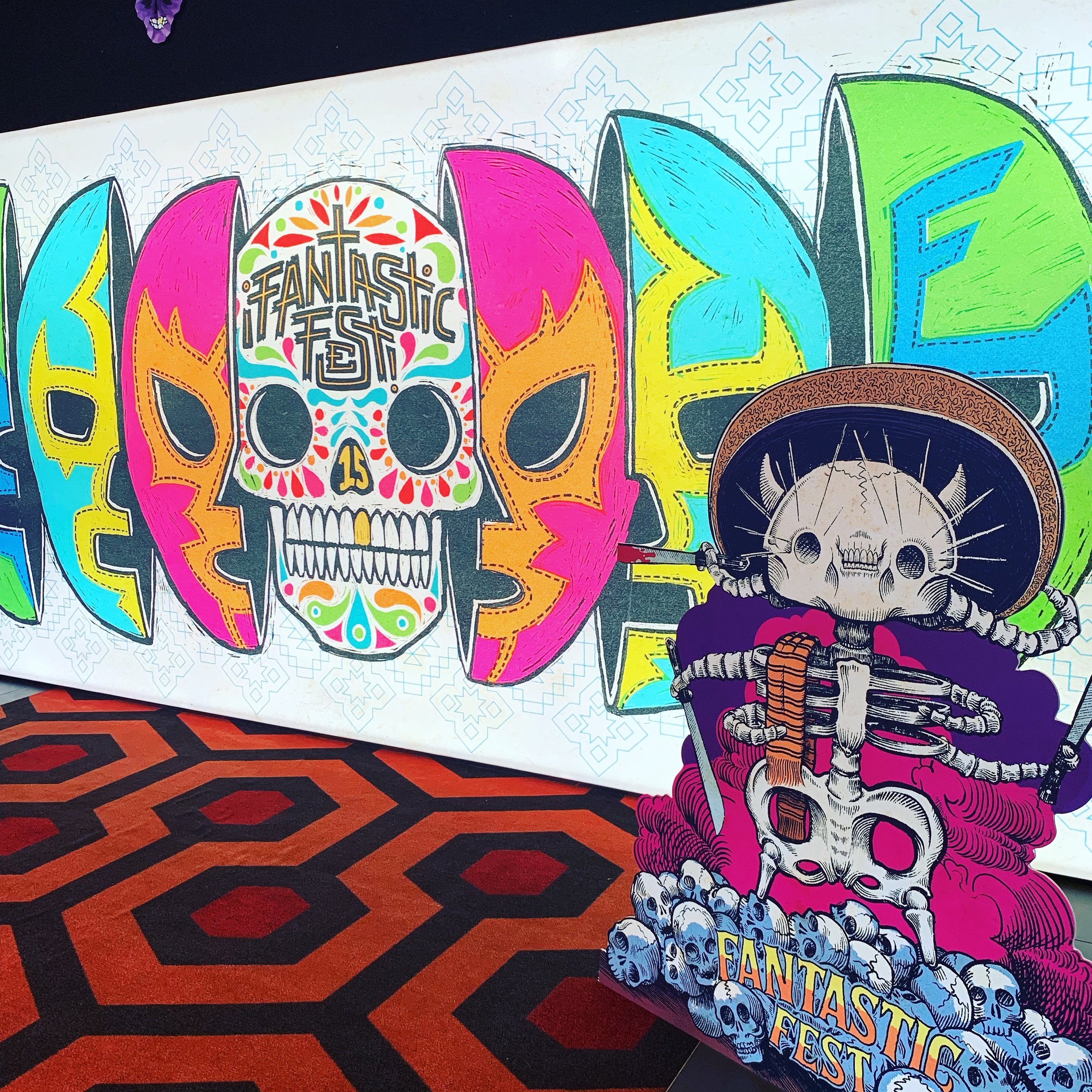 Colorful wall art featuring stylized skulls and dragon designs with 'FANTASTIC FEST' written in colorful lettering, on a geometric red and black patterned carpet.