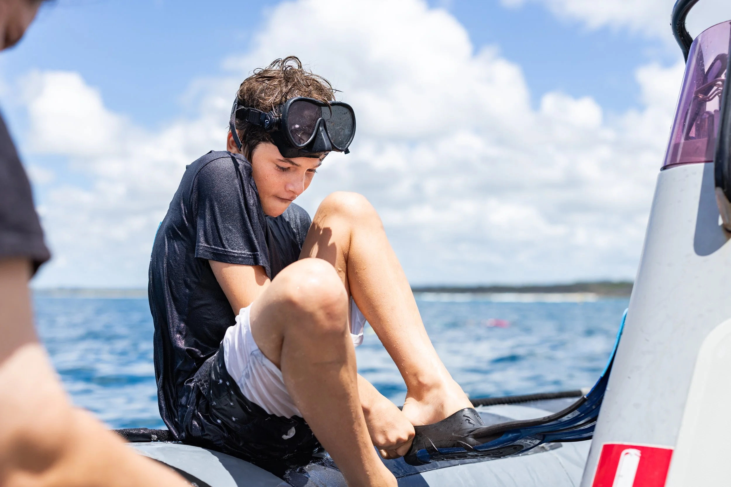 kid sitting on boat and trying on snorkel fins