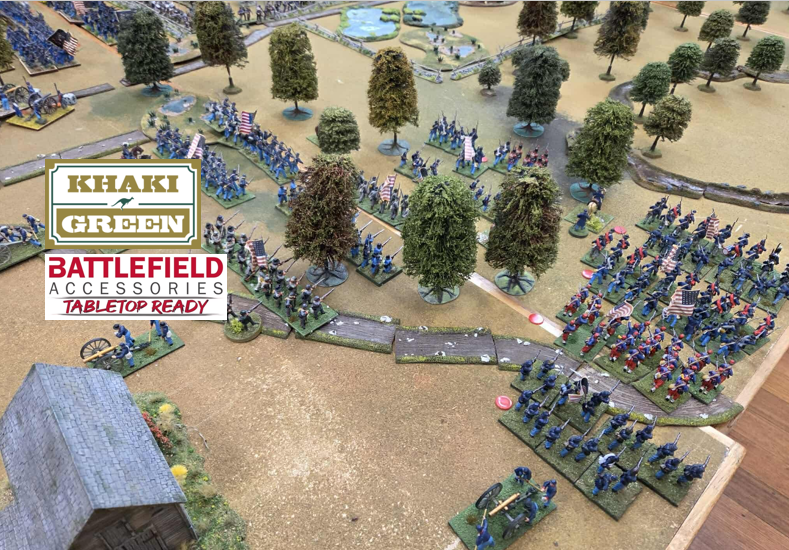 Miniature figures of Union and Confederate soldiers engaged in a battle, set on a tabletop terrain with trees and a small building, depicting a Civil War scene.