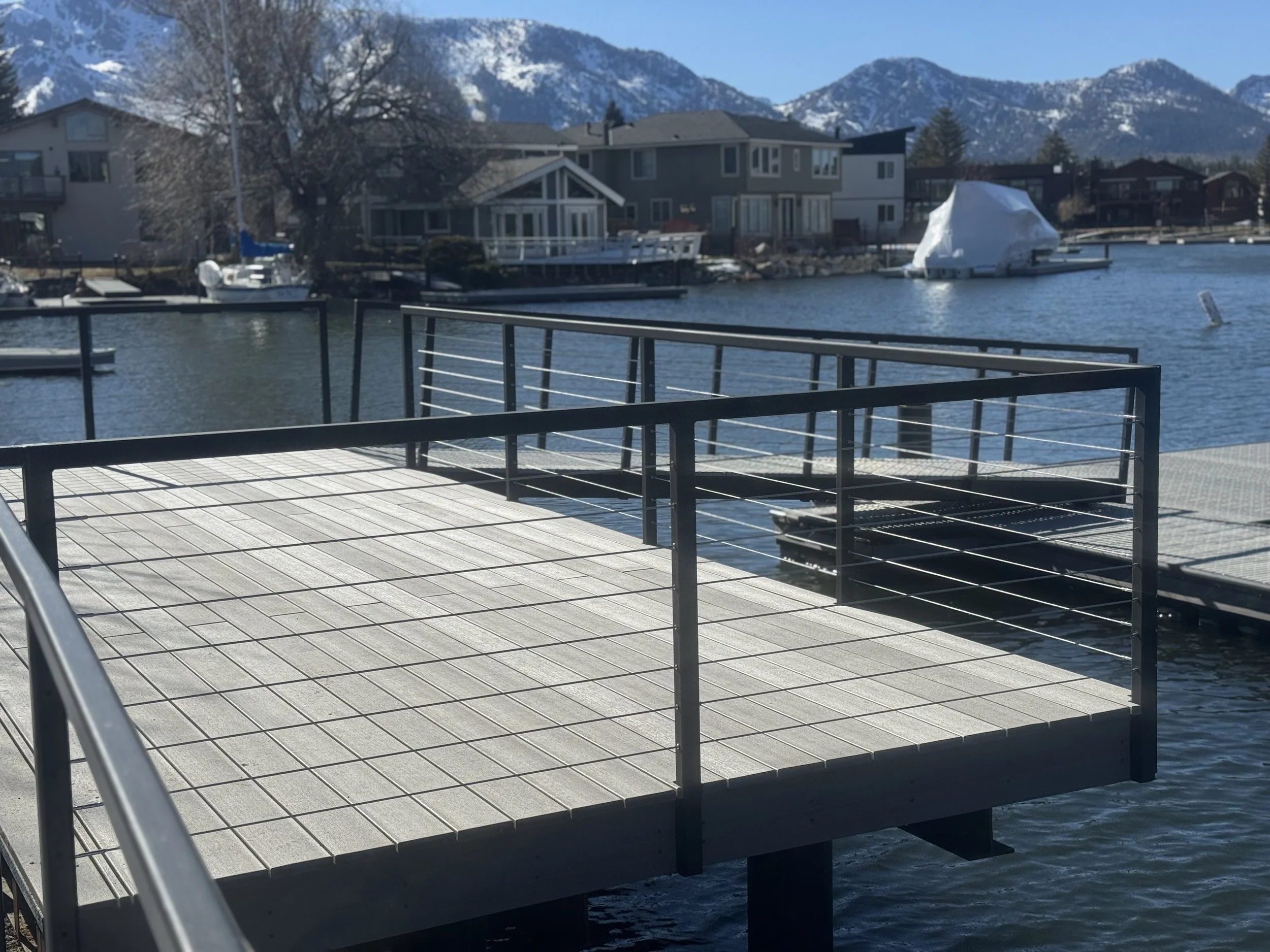 A deck overlooking a lake with boats, houses, and mountains in the background.