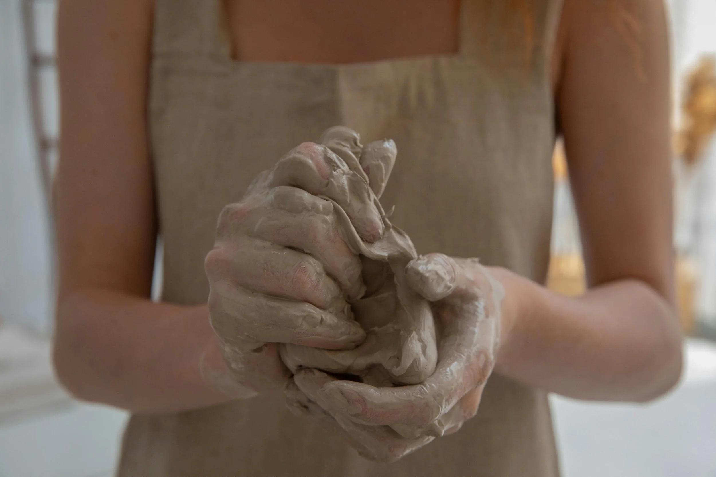 Person wearing a beige apron with hands covered in wet clay.