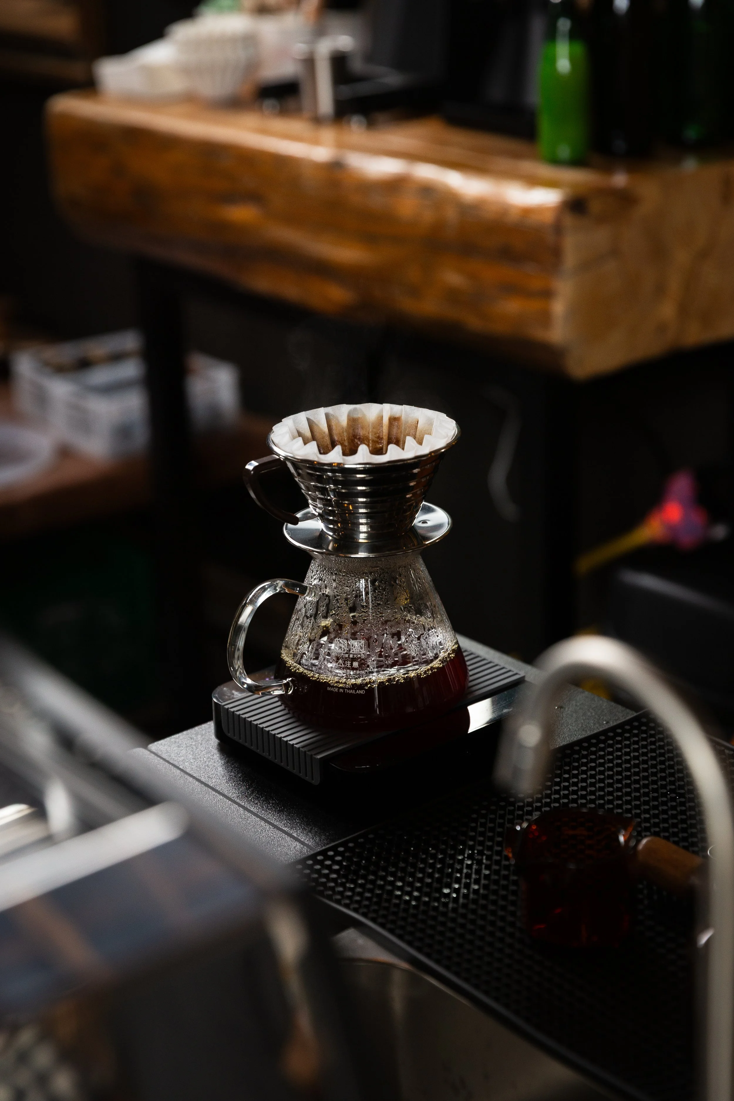 Pour-over coffee maker with dark brewed coffee on a black scale, in a cafe or kitchen setting.