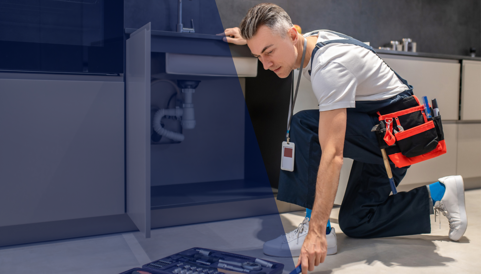 A repair technician kneeling on the floor, working under a kitchen sink, with tools in a red and black tool bag attached to his waist.