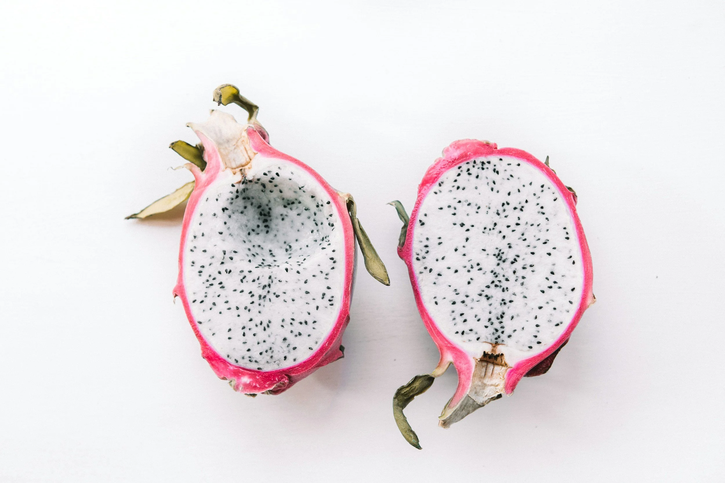 Halved dragon fruit showing white flesh with black seeds and pink skin