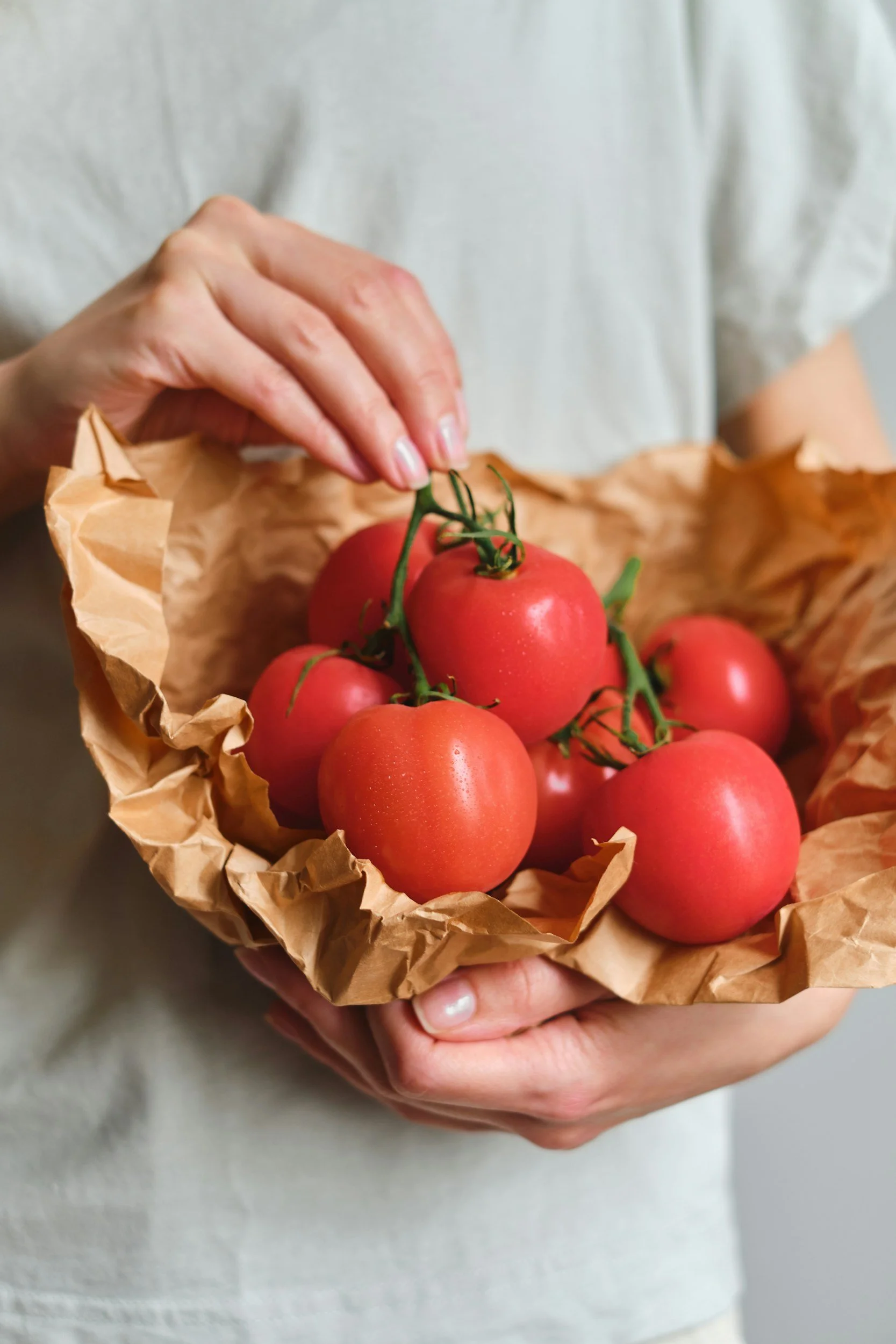 Person holding a paper-lined basket of fresh, ripe tomatoes.