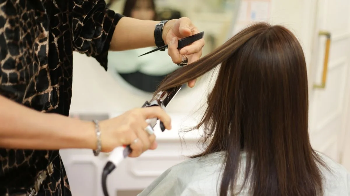 A hairstylist straightening a woman's brown hair with a flat iron in a salon.