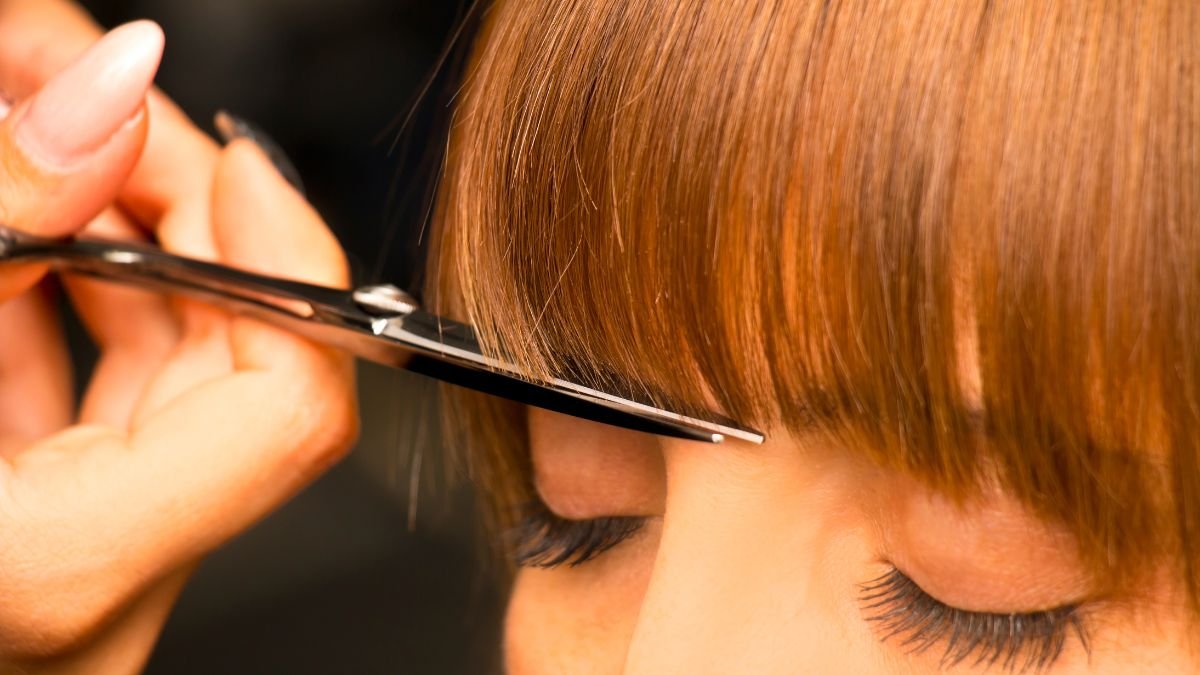 Close-up of a person getting a haircut with scissors, focusing on their freshly cut, reddish-brown hair and closed eyes.