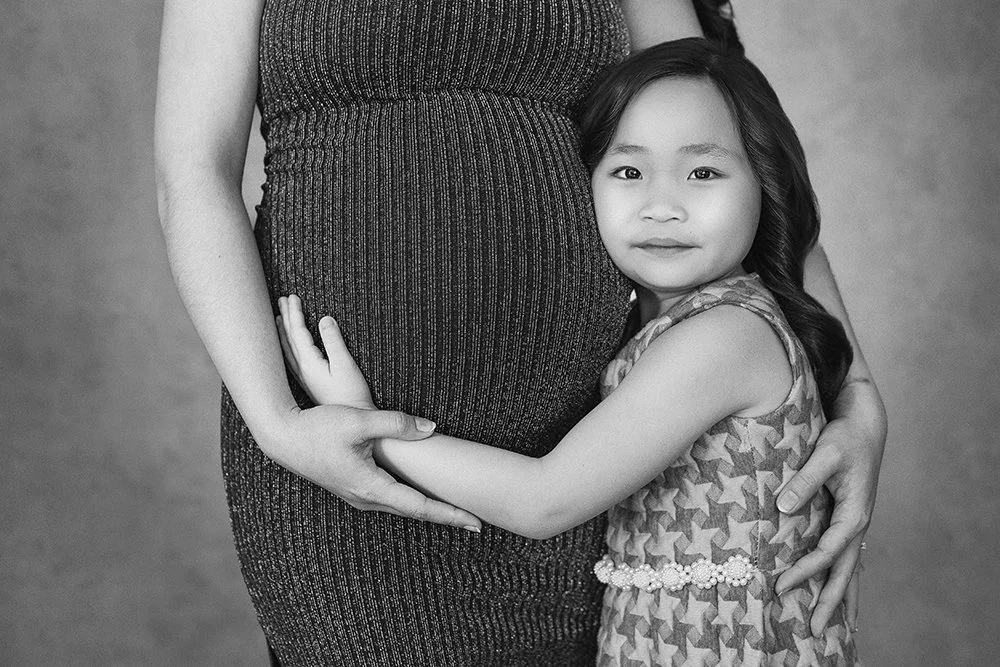A young girl hugging a pregnant woman's belly, both looking at the camera.