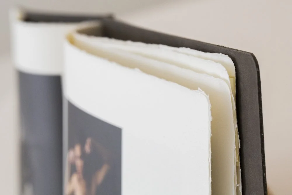 Close-up of two books standing upright with visible pages, one with a black cover and the other with a white cover, against a neutral background.