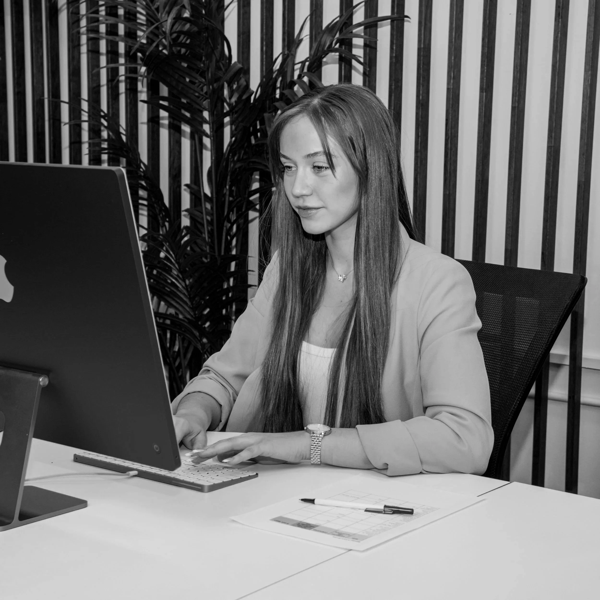 A woman with long hair working on a computer at her desk in an office environment.