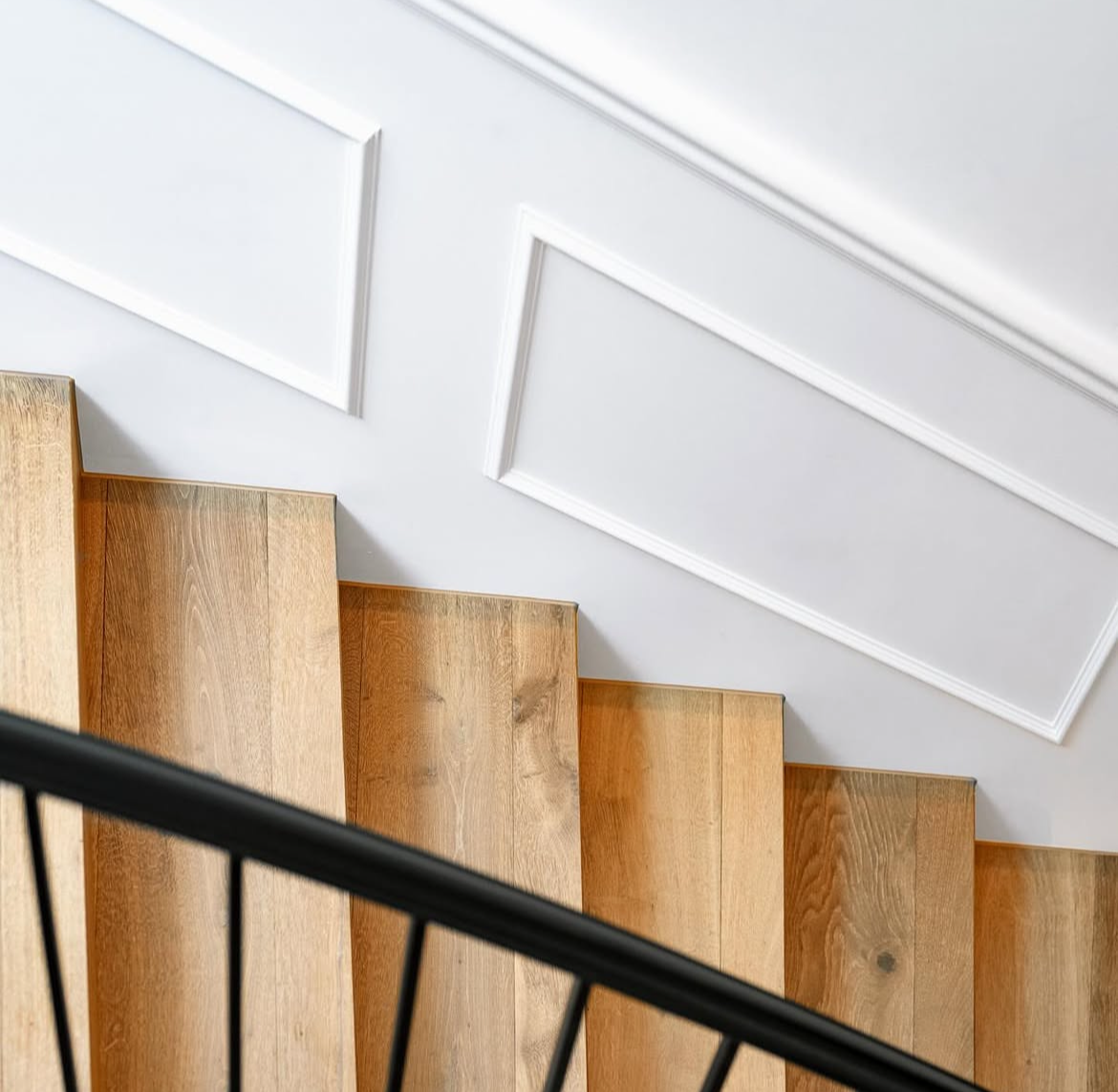 View of a staircase with wooden steps, black railing, and white decorative wall panels on the ceiling.