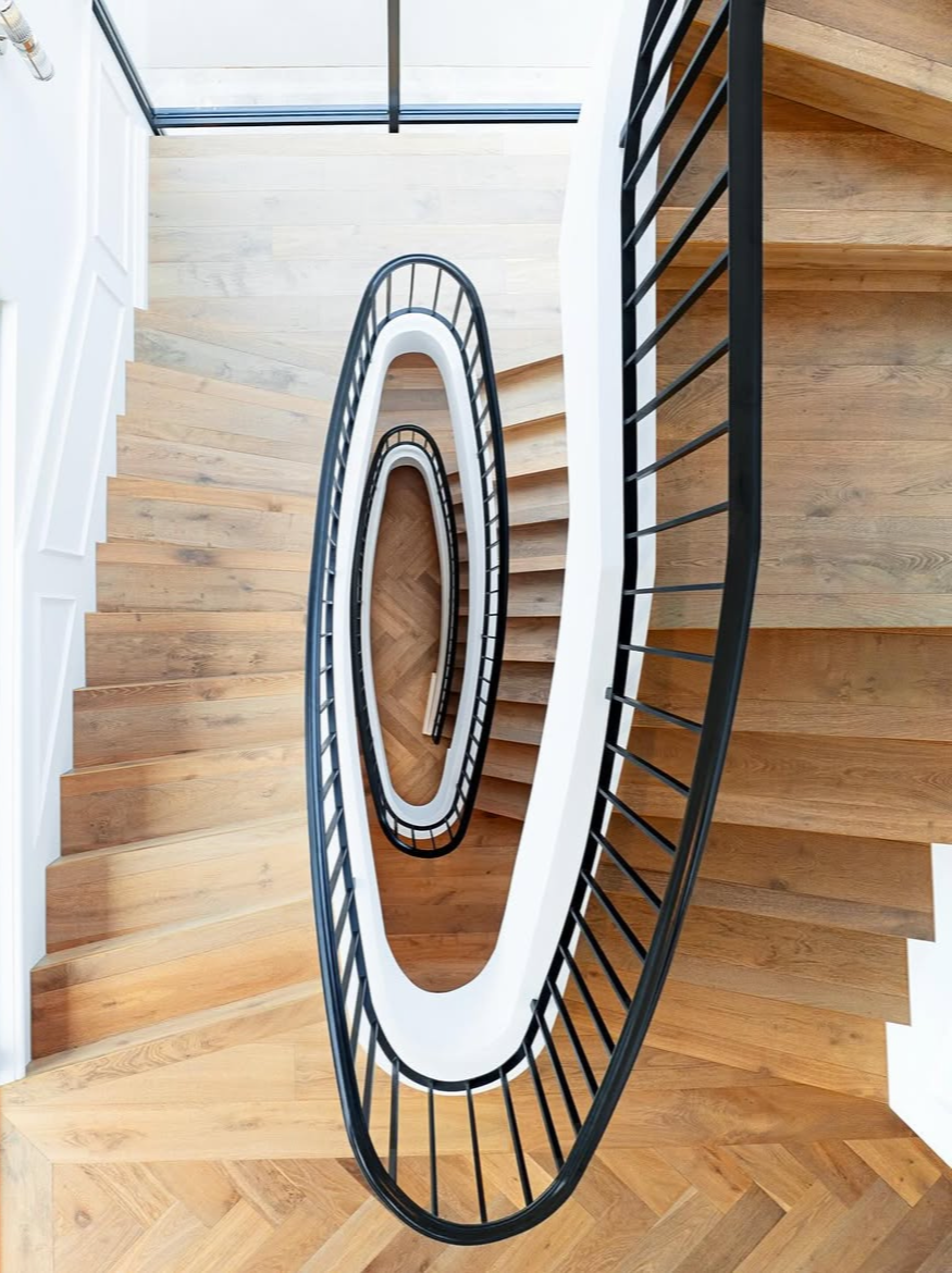Photo looking down a spiral staircase with wooden steps, black railing, and white sides, in a modern building.