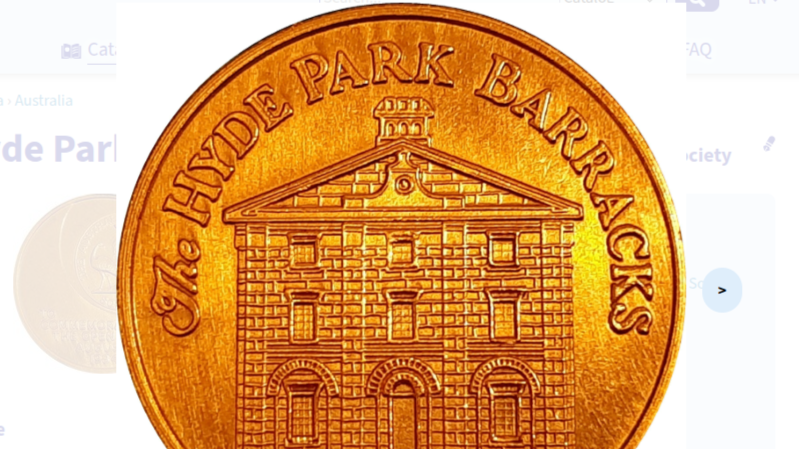 Close-up of a copper coin depicting a historic building and the inscription "The Hyde Park Barracks".
