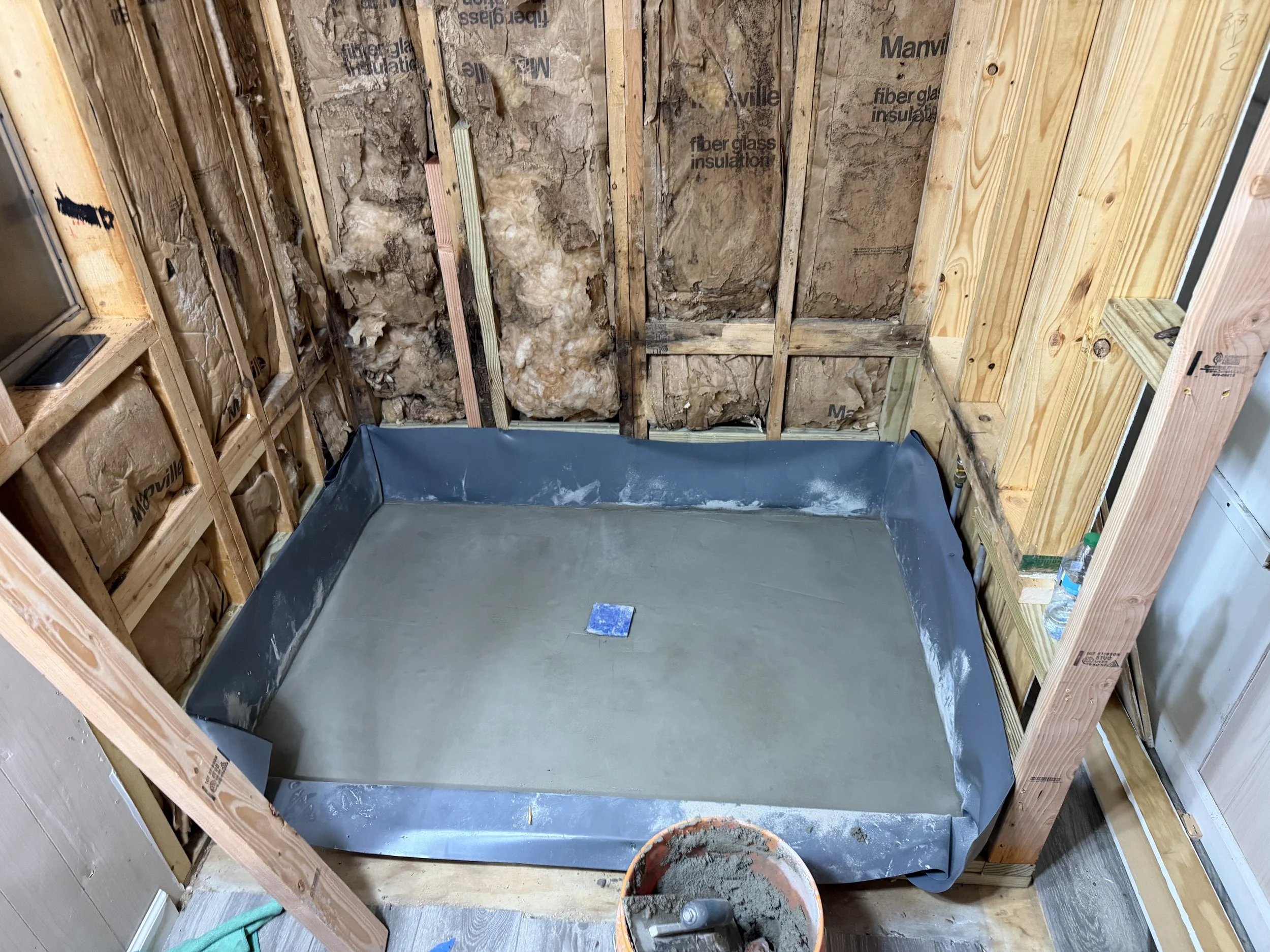 A small bathtub with a gray rubber liner installed in a bathroom under construction, with exposed studs and insulation on the walls.