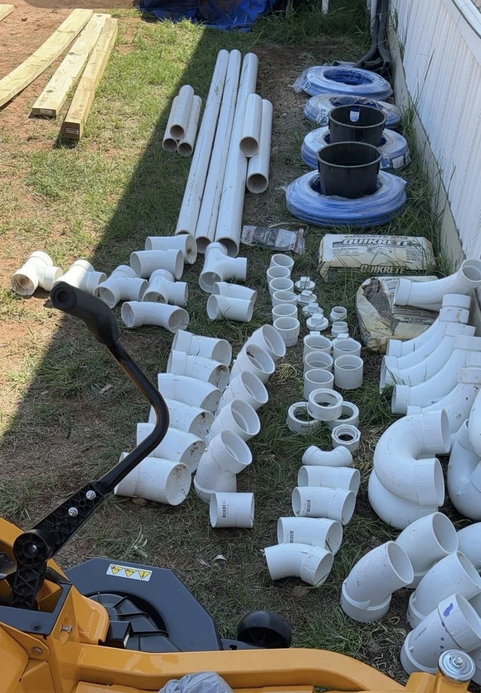 Various PVC pipes, fittings, and construction materials laid out on grass for a building project.