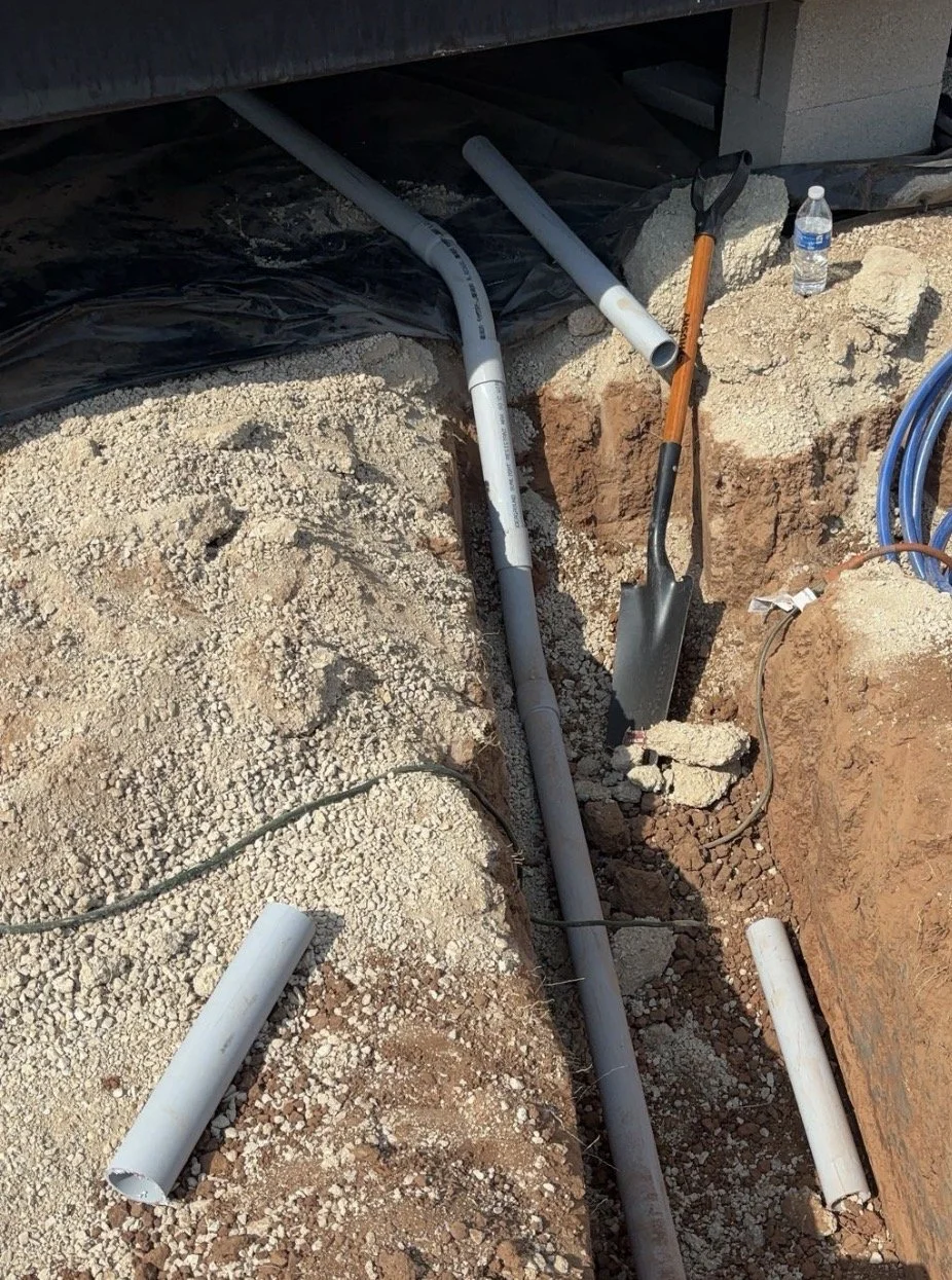 Construction site with PVC pipes, a shovel, a water bottle, and exposed soil.