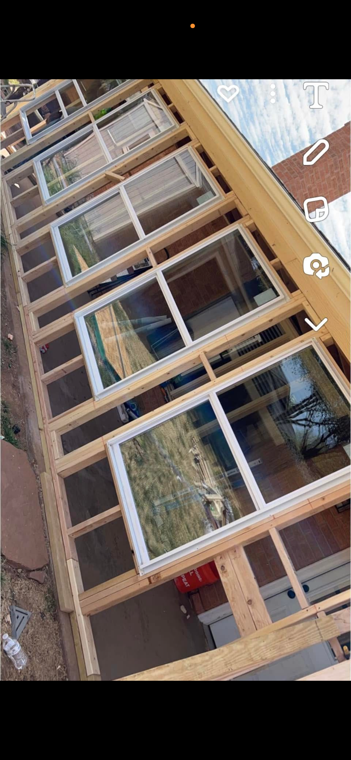 Construction of a wooden-framed structure with multiple large windows with white frames, part of a building under construction.