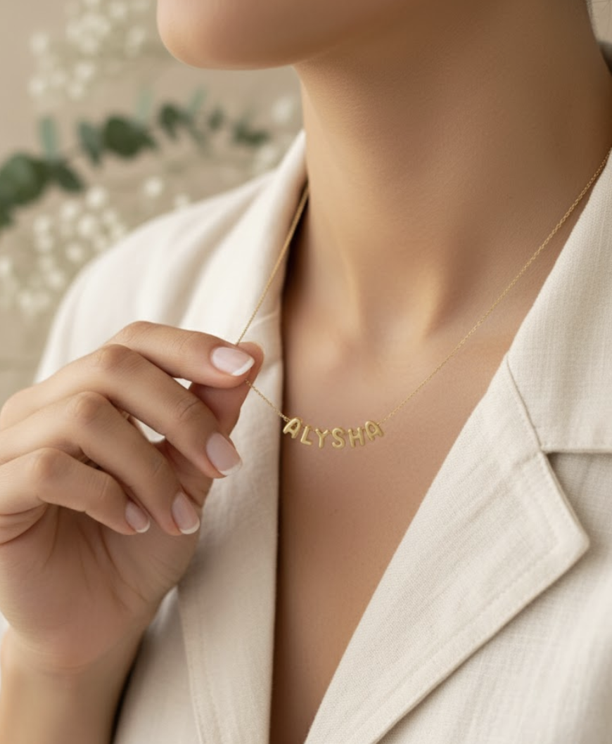 A woman wearing a white blazer holding a gold necklace with the name 'ALYSHA' in capital letters near her neck.