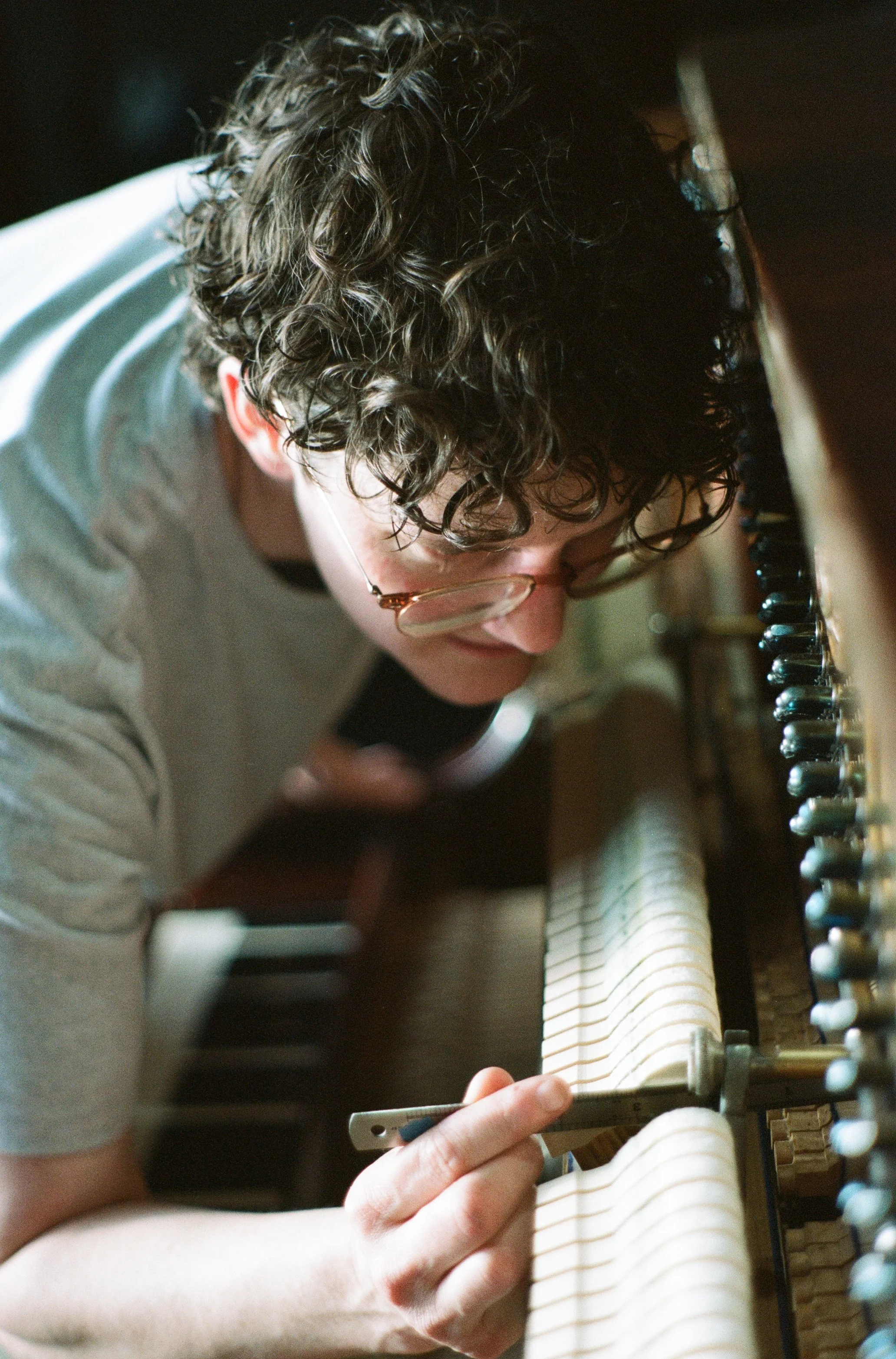 A person with curly hair and glasses tuning a piano.