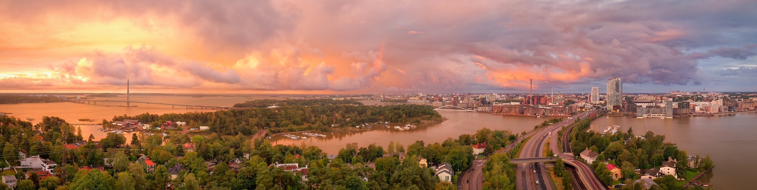 Panoraamakuva Helsingin Kalasatamasta ja tornitaloista ilta-auringon laskun aikaan, kuvattu Kulosaaren suunnasta DJI Air 2S -dronella.