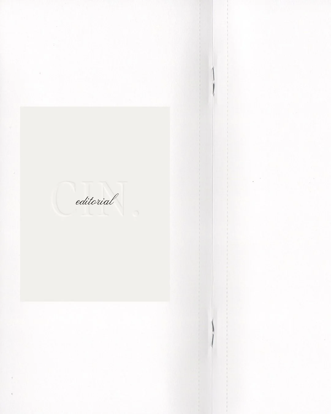 Close-up of a white magazine or book with the word 'CIN.' embossed and 'editorial' written in cursive, on a plain white surface.