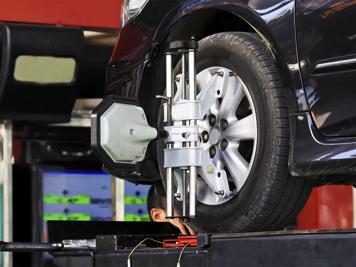 Automotive wheel alignment machine adjusting a car's front wheel on a lift.