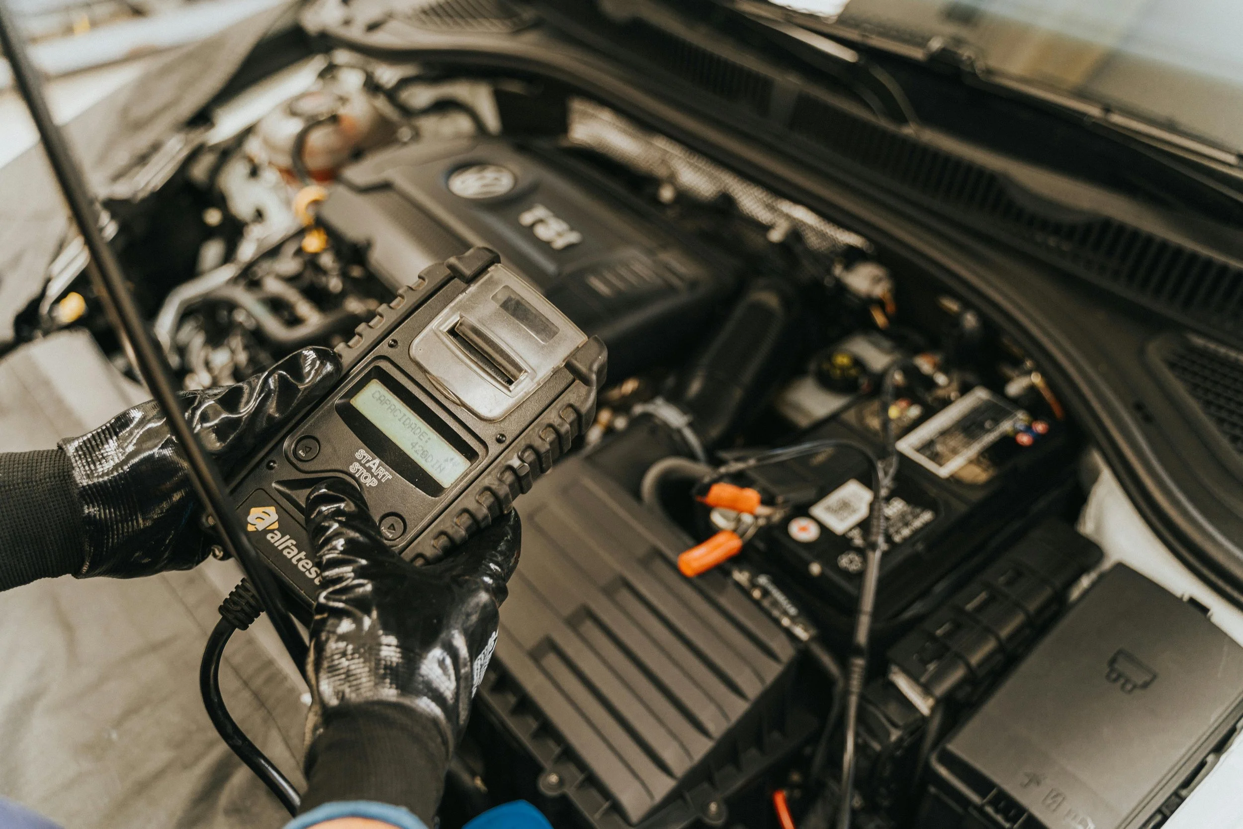 Mechanic using a diagnostic scan tool to check a car's engine under the open hood.