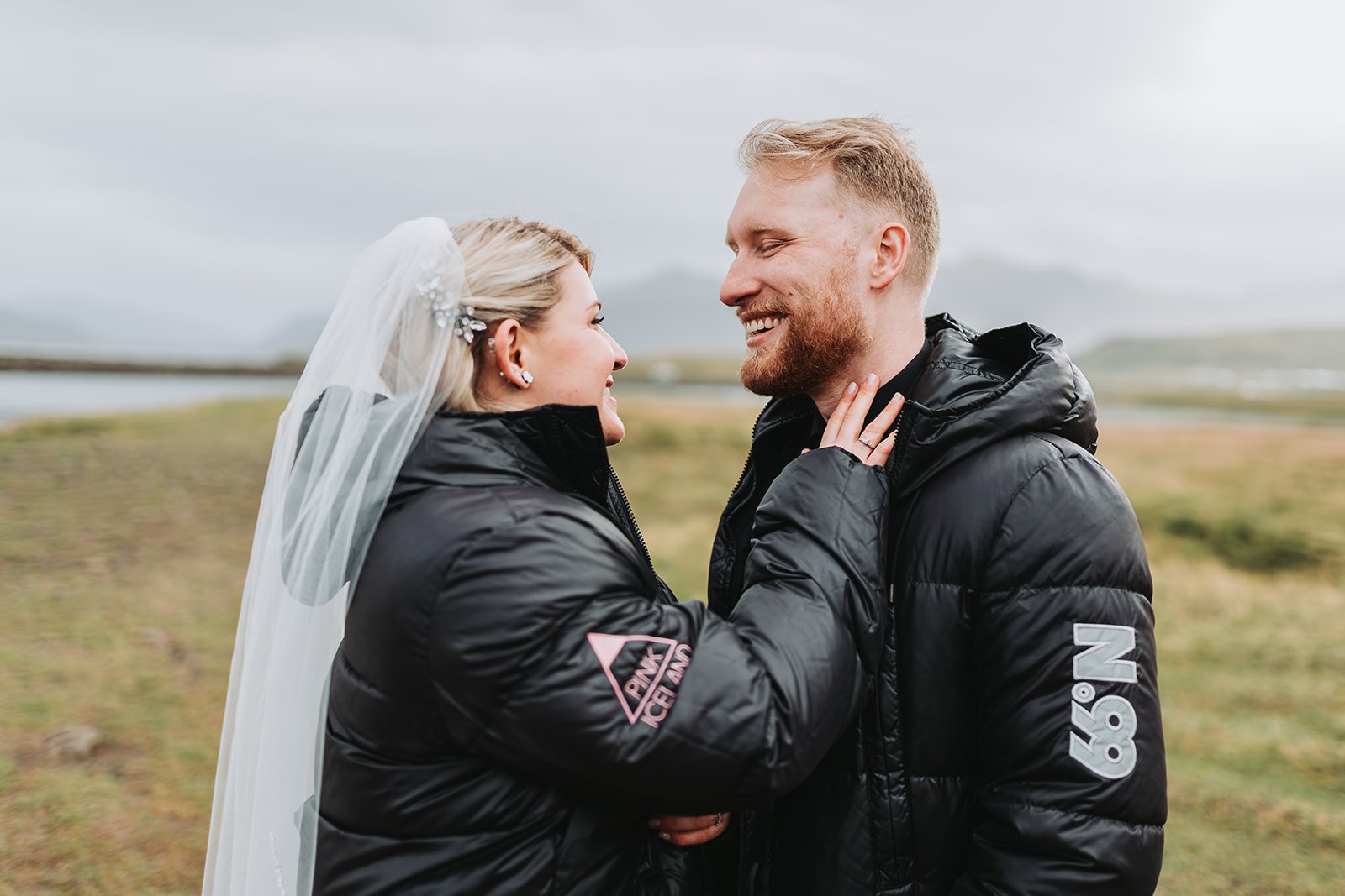 Bride and groom sharing a warm moment in winter jackets during their Iceland elopement on the South Coast, with mountains in the background