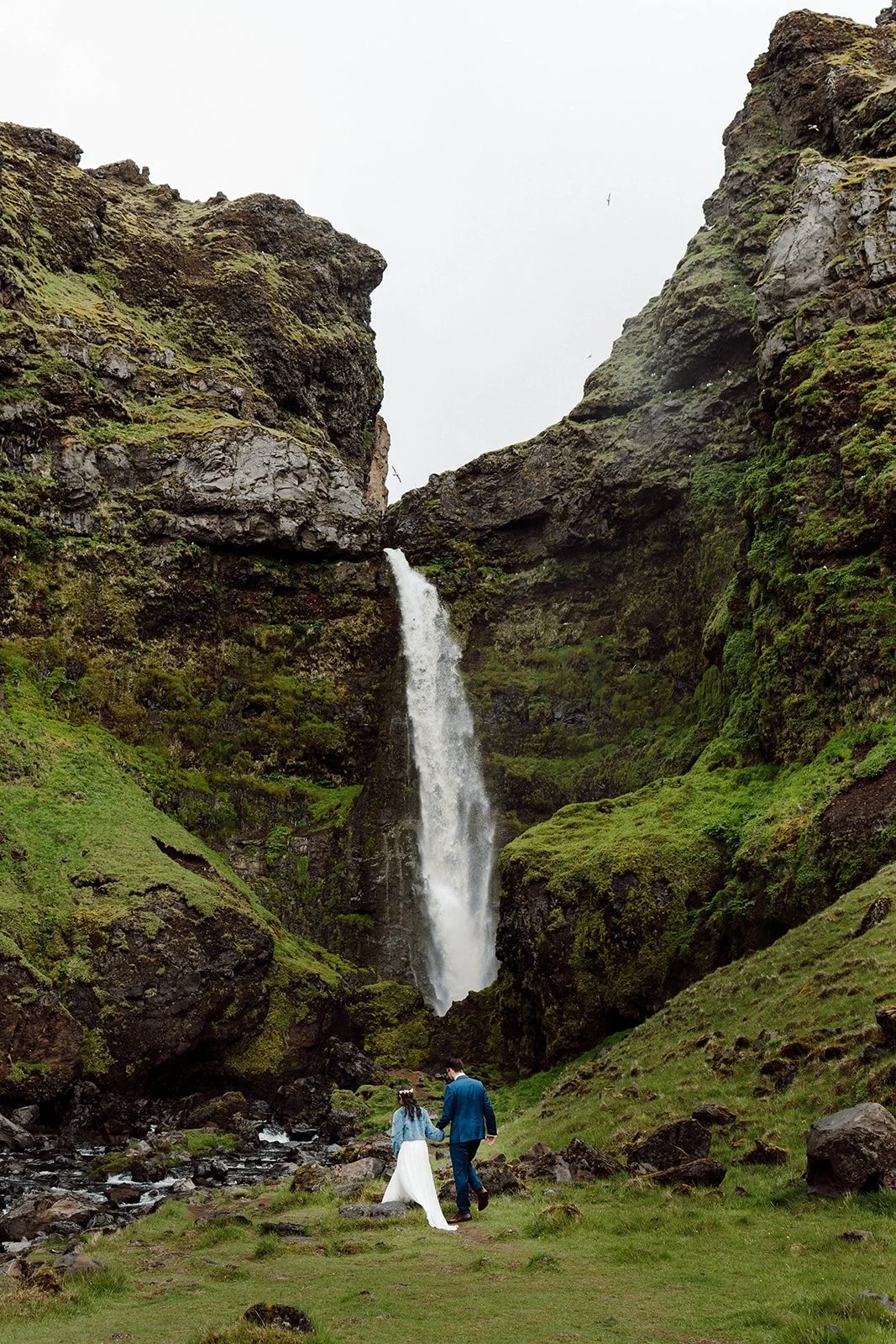 Elopement couple walking toward a waterfall in Iceland surrounded by dramatic cliffs