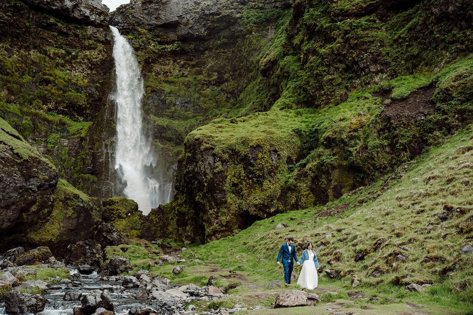 Elopement couple walking hand in hand toward a waterfall in Iceland