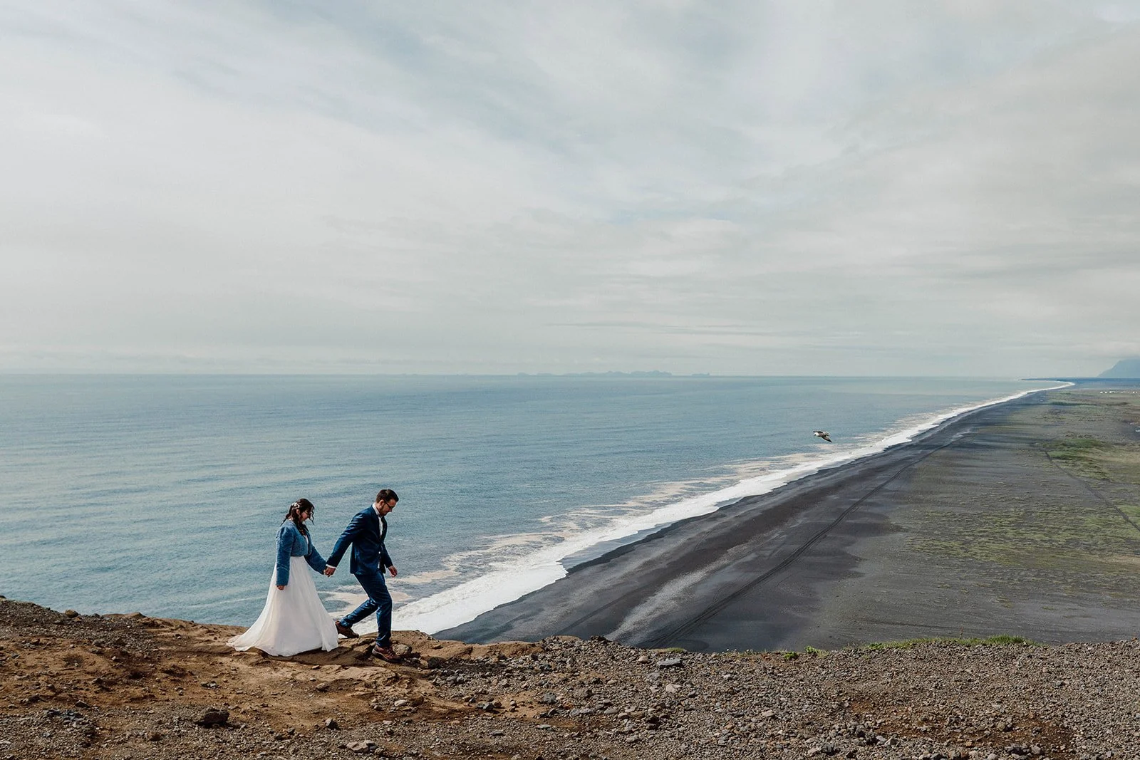 Elopement couple walking along a cliff above Iceland’s black sand beach