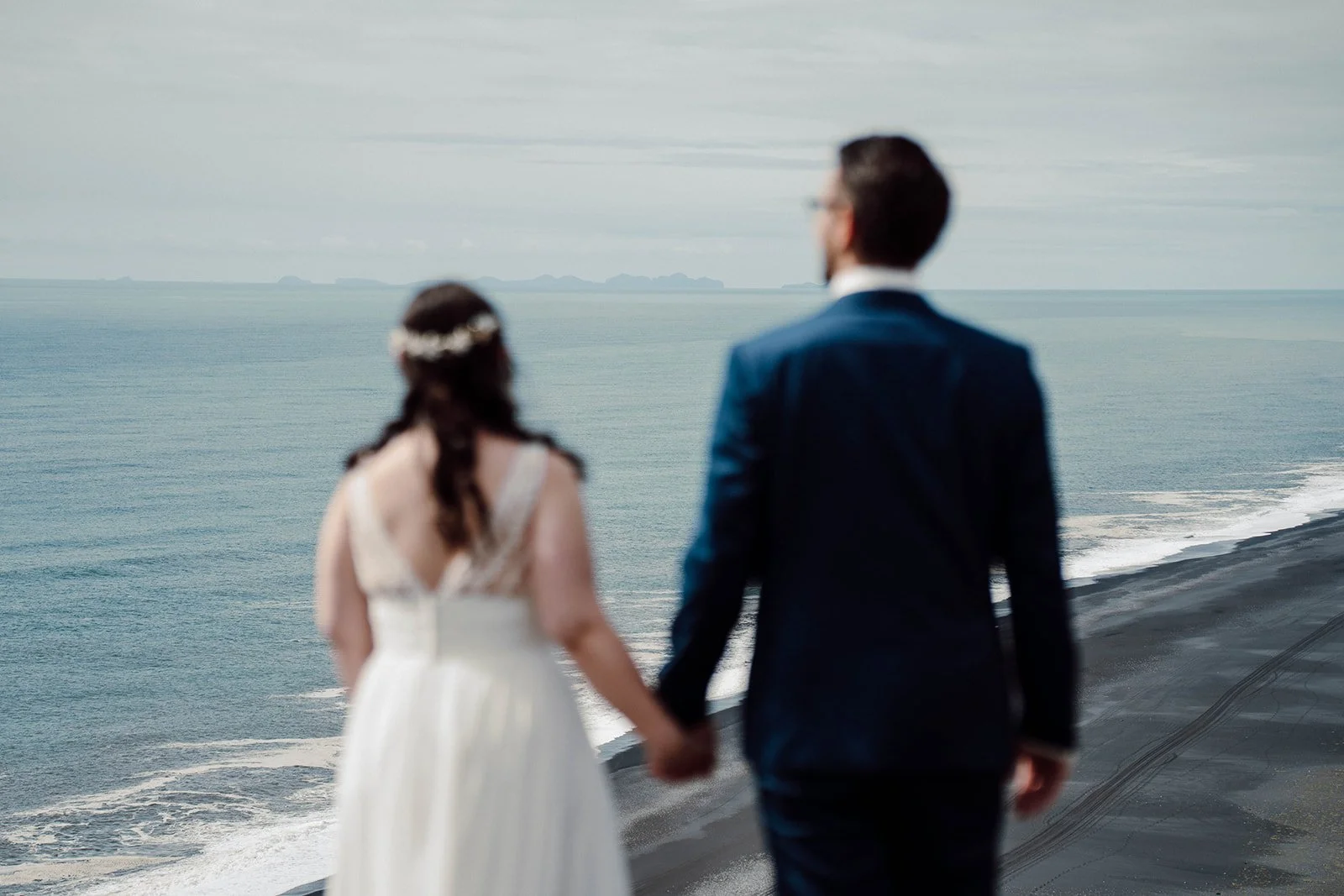 Elopement couple walking hand in hand on a cliff above Iceland’s black sand beach