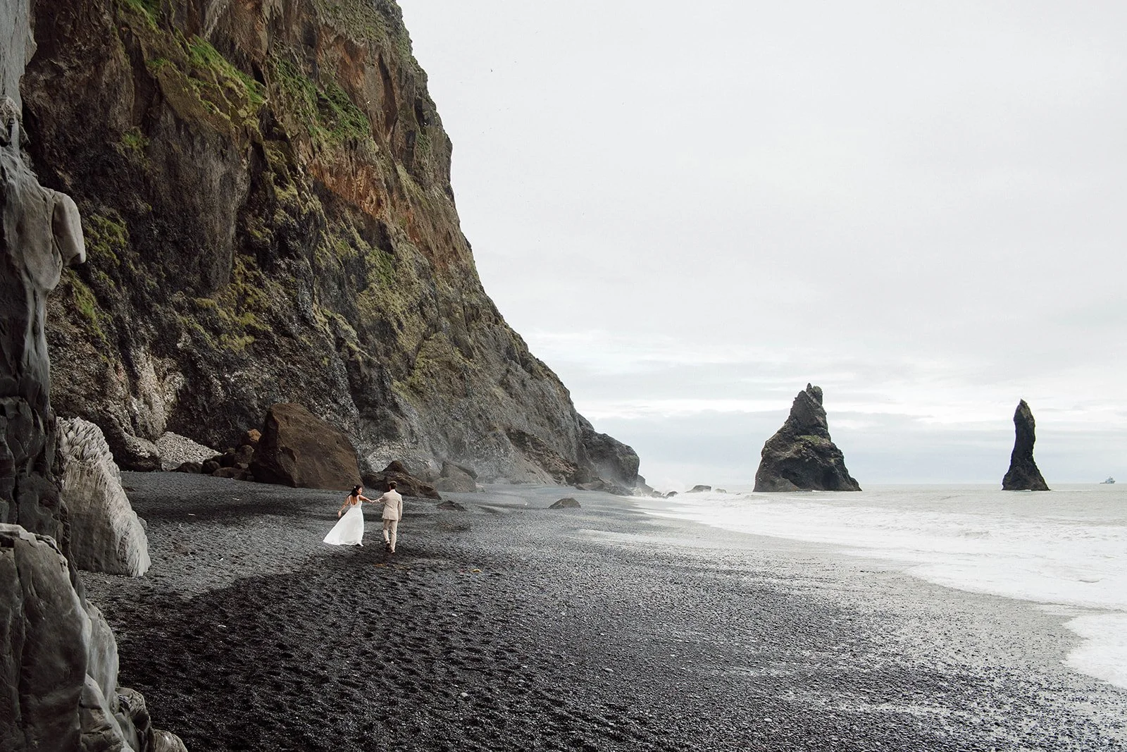 Couple running on the black sand beach with Reynisdrangar sea stacks in Vík, Iceland — Iceland elopement photographer