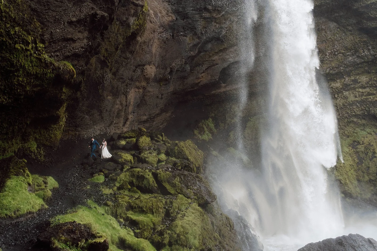 Couple walking behind Seljalandsfoss waterfall during Iceland elopement