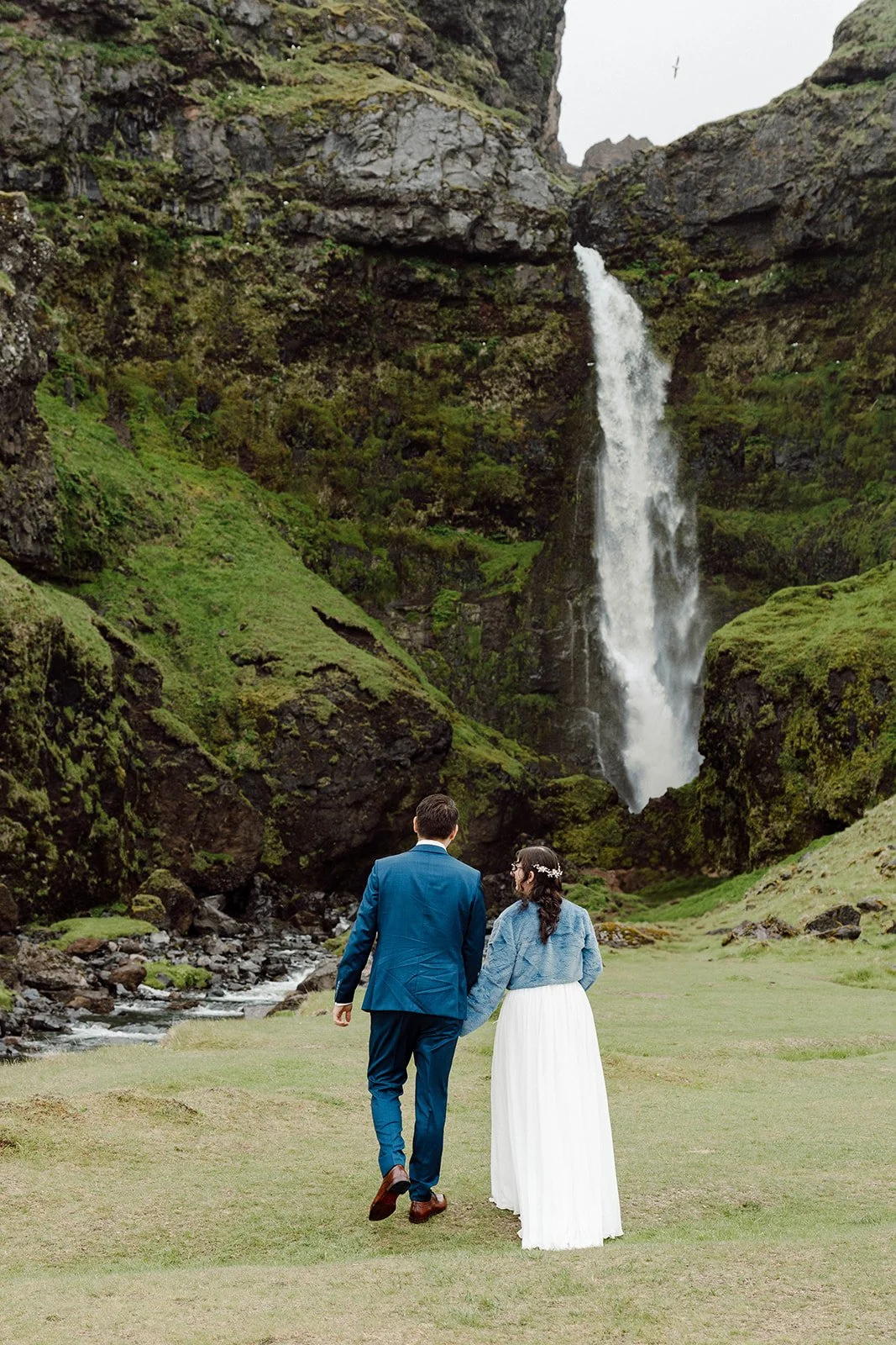 Bride and groom walking toward a dramatic waterfall during their adventure elopement in Iceland