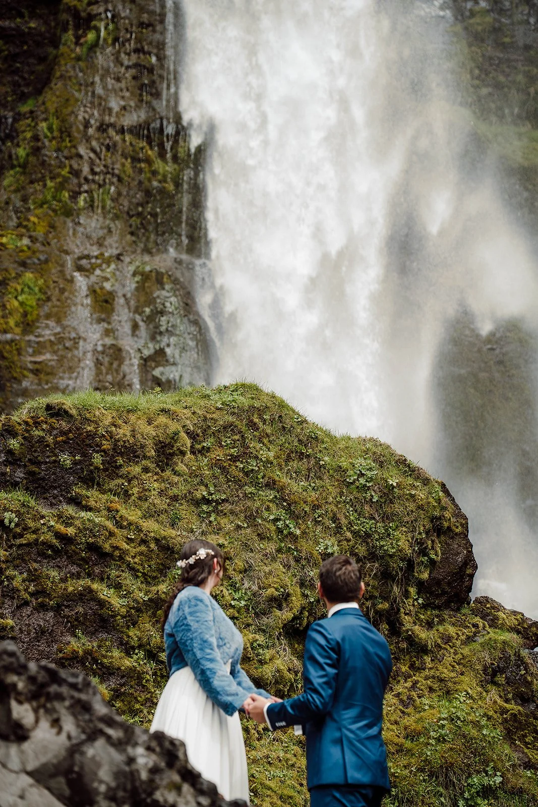 Elopement couple holding hands near a powerful waterfall in Iceland