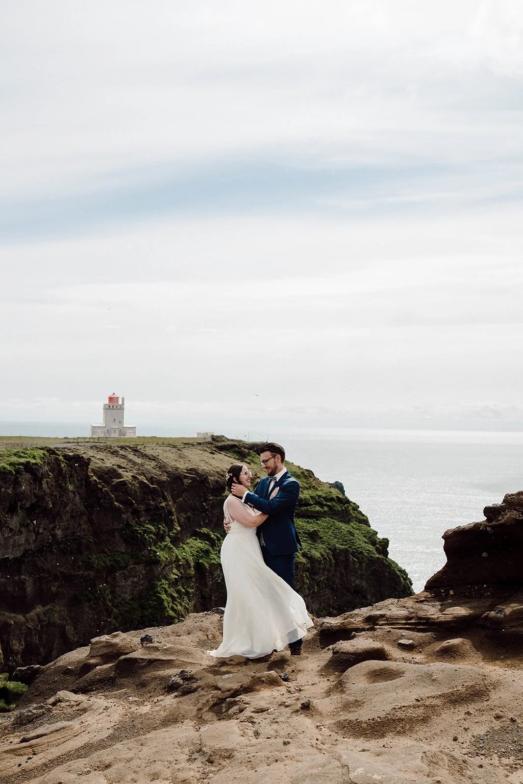 Elopement couple embracing near lighthouse on Iceland cliffs