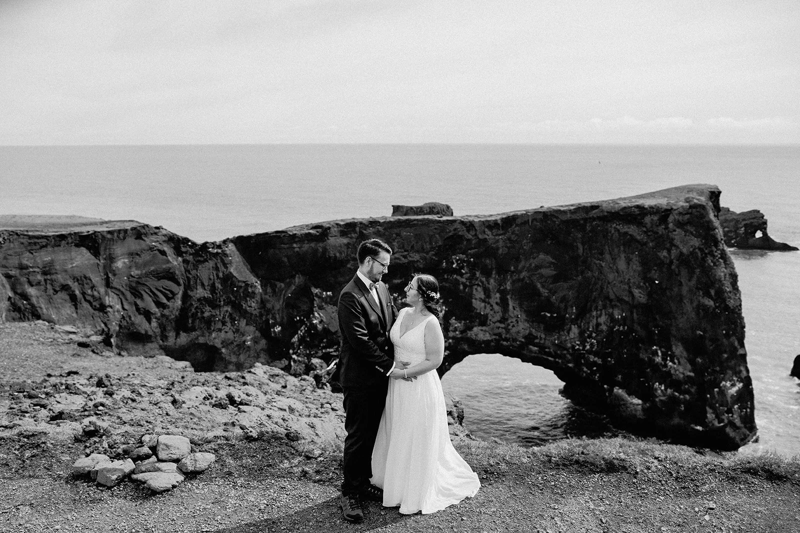 Black and white photo of elopement couple standing by a rock arch cliff in Iceland