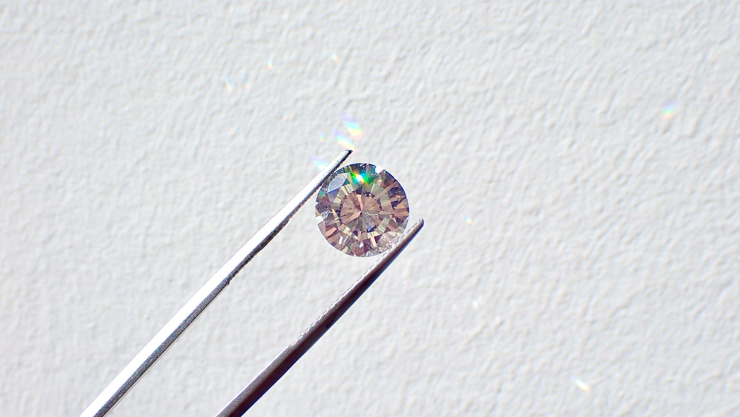 A round brilliant-cut diamond held by tweezers against a white background.