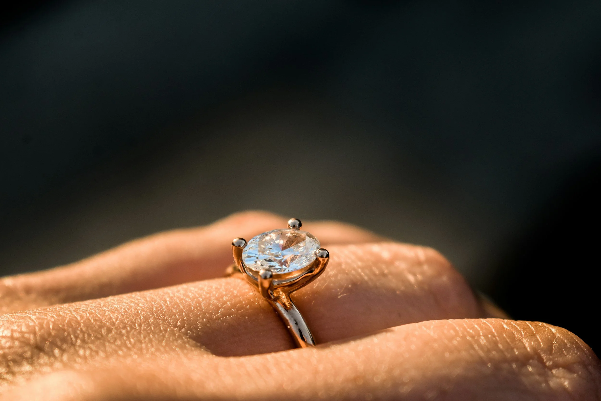 Close-up of a person's finger wearing a silver ring with a large, round, faceted diamond.