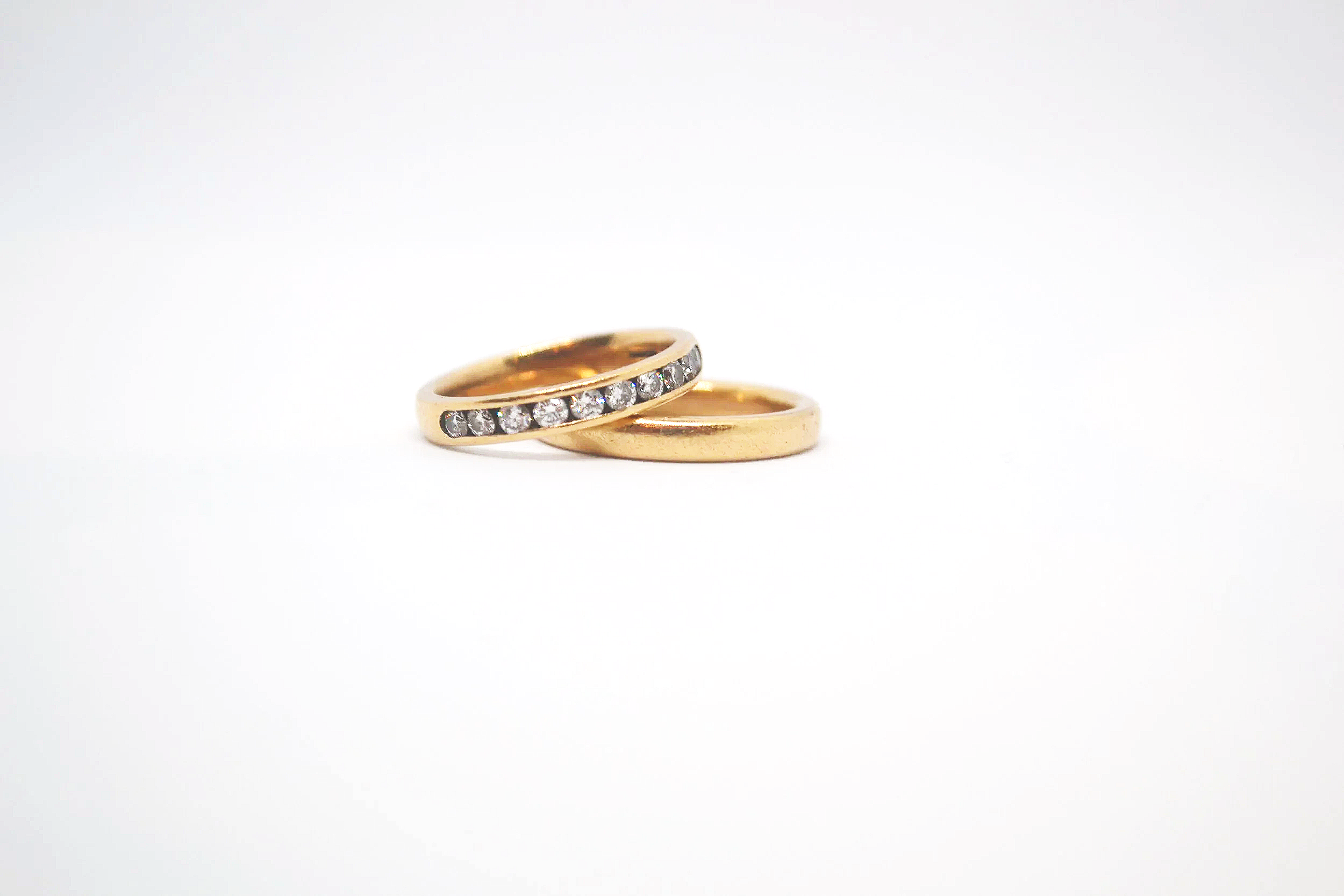 Two gold rings, one with diamonds, placed on a white background.