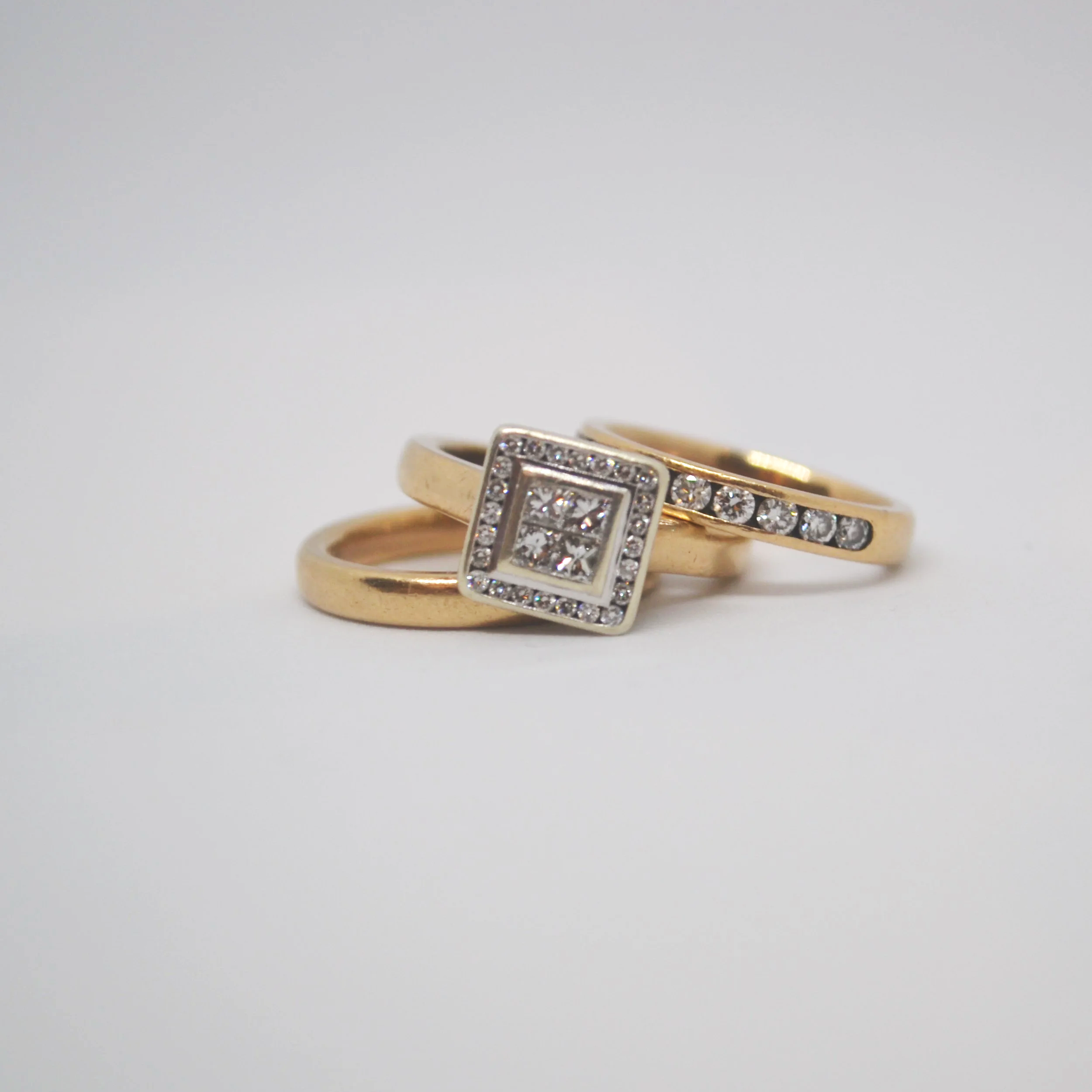 Gold rings, one with a square diamond, and two with accent diamonds, on a white background.
