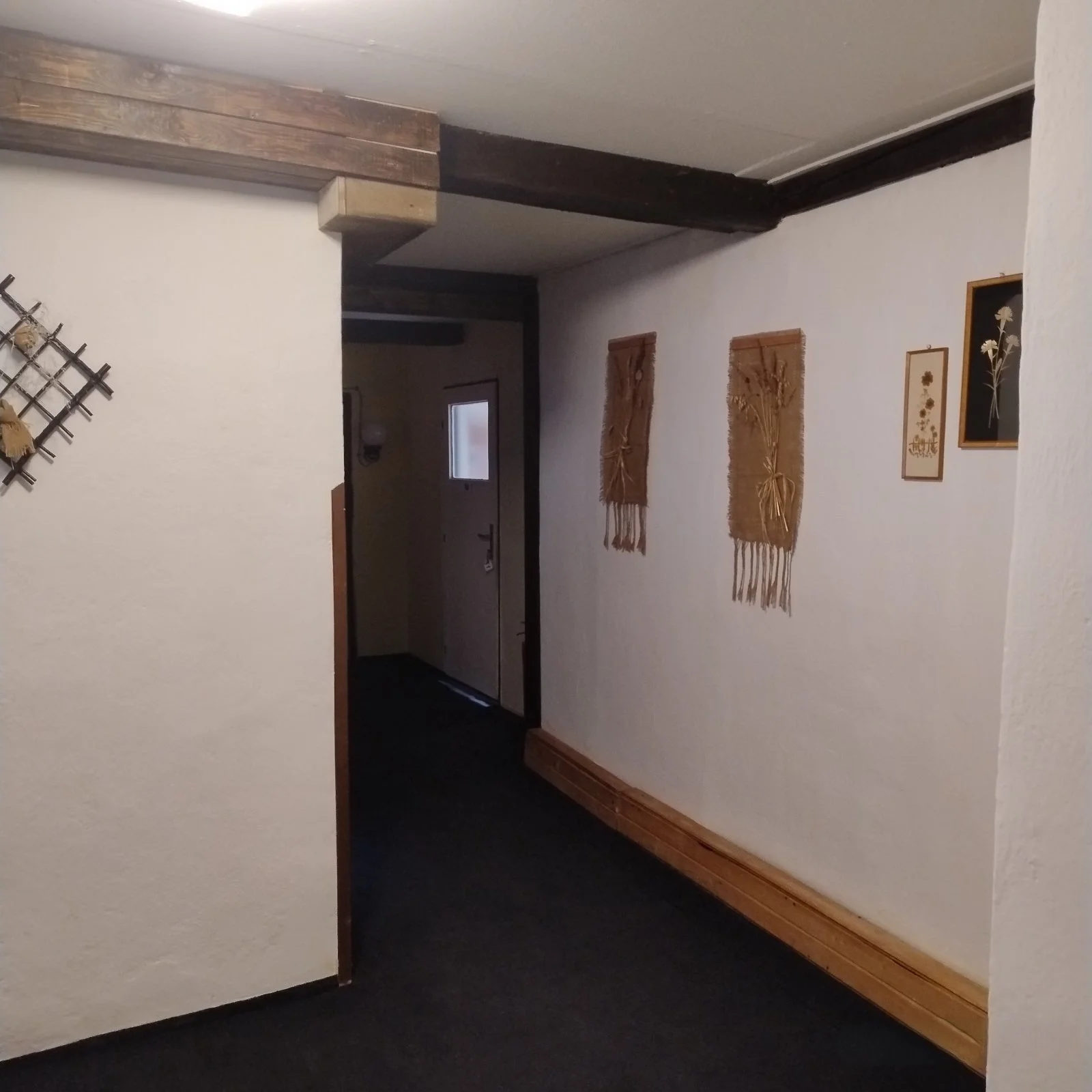 Interior hallway with white walls, wooden wall decorations, and a dark carpeted floor.