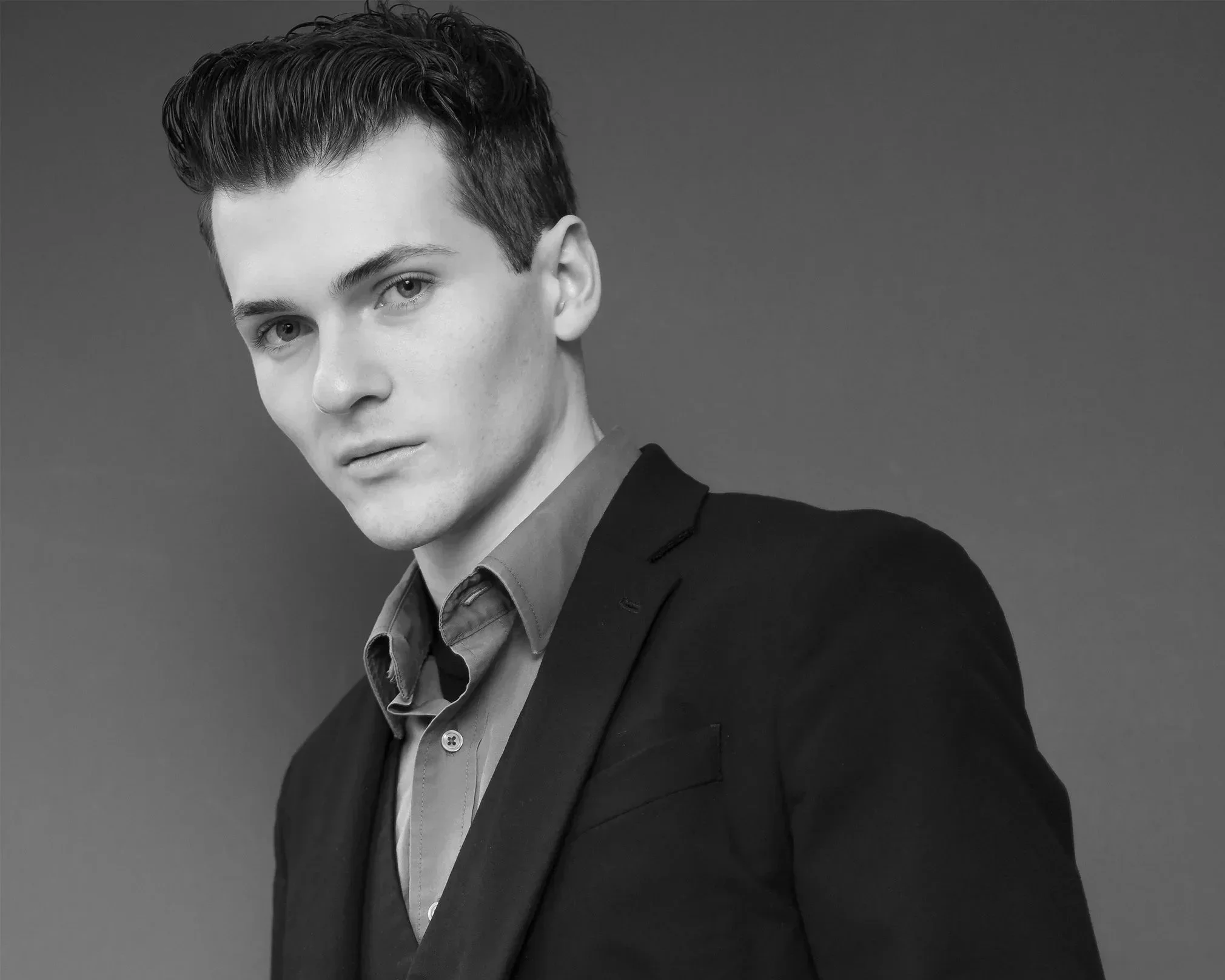 A black and white portrait of Benjamin Rocha in a suit jacket and shirt, looking directly into the camera with a serious expression.