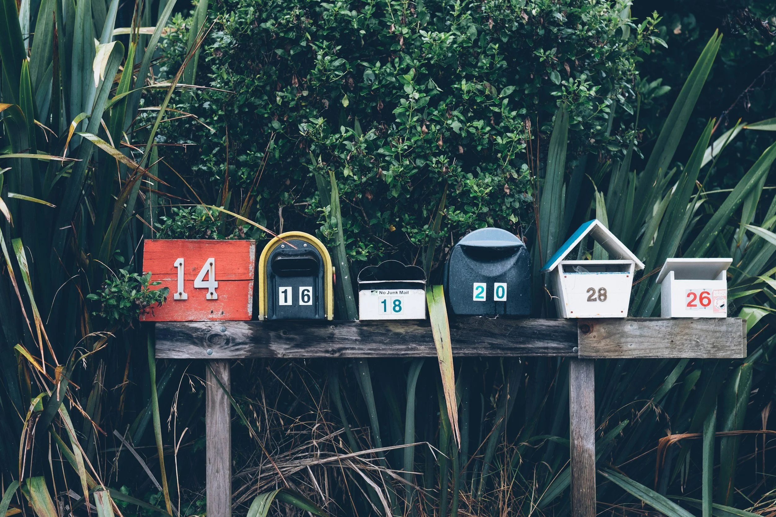 A row of six different mailboxes on a wooden stand, symbolizing communication and connection.