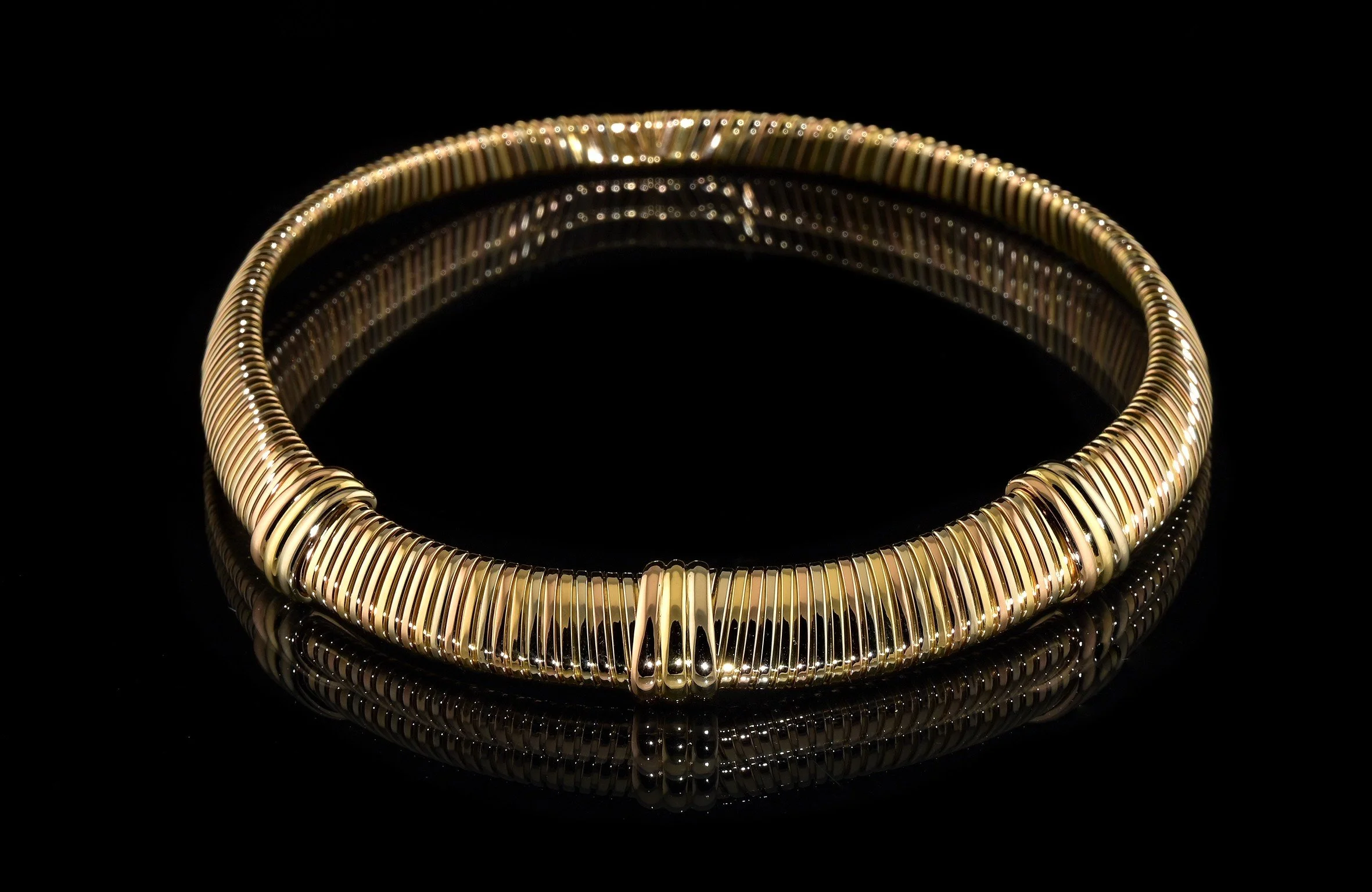 Un tas de bijoux en or avec des pierres colorées rouges et bleues, posés sur un fond noir